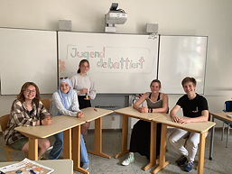 Das Foto zeigt fünf AG-Teilnehmer an Schultischen vor einem Whiteboard mit der Anschrift 'Jugend gebattiert'.