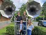 Das Foto zeigt die vier Schülerinnen und Schüler des TGG vor und innerhalb einer Metallinstallation mit zwei Lautsprechern oder Hörrohren.